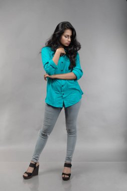 Gri arka plan karşısında gündelik giyimli Hintli genç manken. Stok fotoğrafı. Uzun siyah saç modeli mavi gömlek giyiyor..