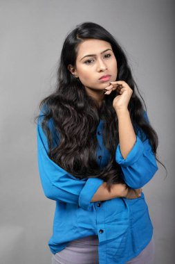 Gri arka plan karşısında gündelik giyimli Hintli genç manken. Stok fotoğrafı. Uzun siyah saç modeli mavi gömlek giyiyor..