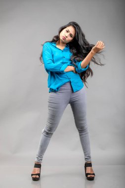 Gri arka plan karşısında gündelik giyimli Hintli genç manken. Stok fotoğrafı. Uzun siyah saç modeli mavi gömlek giyiyor..