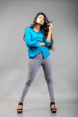 Gri arka plan karşısında gündelik giyimli Hintli genç manken. Stok fotoğrafı. Uzun siyah saç modeli mavi gömlek giyiyor..