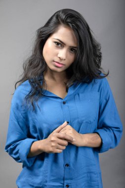 Gri arka plan karşısında gündelik giyimli Hintli genç manken. Stok fotoğrafı. Uzun siyah saç modeli mavi gömlek giyiyor..