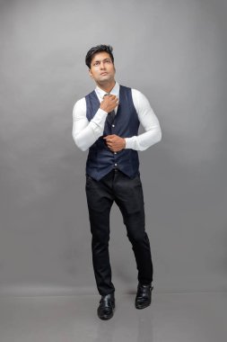 Gri arka planda resmi giyinmiş neşeli, genç ve yakışıklı Hintli iş adamının stüdyo çekimi. Erkek model. Moda Portresi.