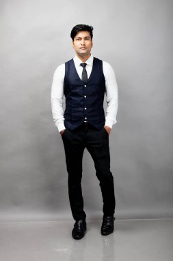 Gri arka planda resmi giyinmiş neşeli, genç ve yakışıklı Hintli iş adamının stüdyo çekimi. Erkek model. Moda Portresi.