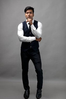 Gri arka planda resmi giyinmiş neşeli, genç ve yakışıklı Hintli iş adamının stüdyo çekimi. Erkek model. Moda Portresi.