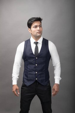 Gri arka planda resmi giyinmiş neşeli, genç ve yakışıklı Hintli iş adamının stüdyo çekimi. Erkek model. Moda Portresi.