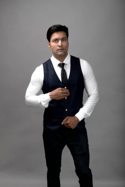 Gri arka planda resmi giyinmiş neşeli, genç ve yakışıklı Hintli iş adamının stüdyo çekimi. Erkek model. Moda Portresi.