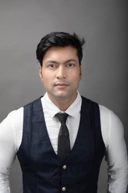 Gri arka planda resmi giyinmiş neşeli, genç ve yakışıklı Hintli iş adamının stüdyo çekimi. Erkek model. Moda Portresi.