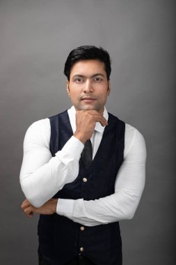 Gri arka planda resmi giyinmiş neşeli, genç ve yakışıklı Hintli iş adamının stüdyo çekimi. Erkek model. Moda Portresi.