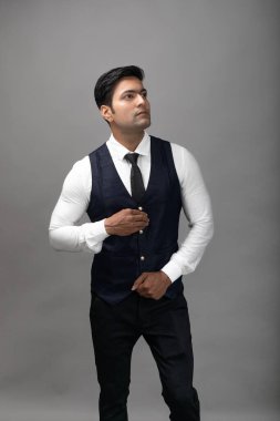 Gri arka planda resmi giyinmiş neşeli, genç ve yakışıklı Hintli iş adamının stüdyo çekimi. Erkek model. Moda Portresi.