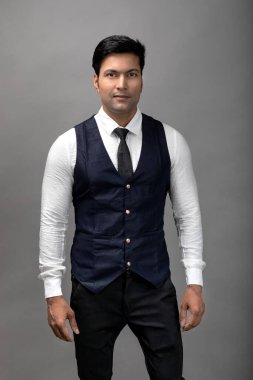 Gri arka planda resmi giyinmiş neşeli, genç ve yakışıklı Hintli iş adamının stüdyo çekimi. Erkek model. Moda Portresi.