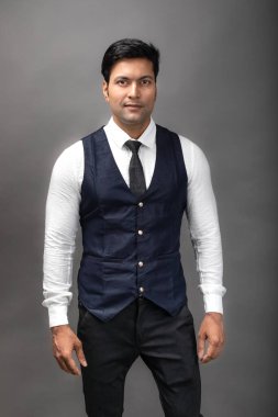 Gri arka planda resmi giyinmiş neşeli, genç ve yakışıklı Hintli iş adamının stüdyo çekimi. Erkek model. Moda Portresi.