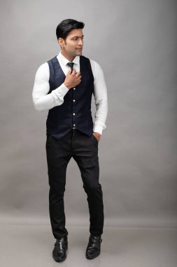 Gri arka planda resmi giyinmiş neşeli, genç ve yakışıklı Hintli iş adamının stüdyo çekimi. Erkek model. Moda Portresi.