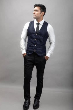 Gri arka planda resmi giyinmiş neşeli, genç ve yakışıklı Hintli iş adamının stüdyo çekimi. Erkek model. Moda Portresi.
