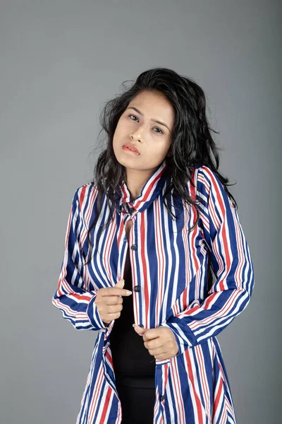 Gri stüdyo arka planında siyah, kırmızı, mavi, beyaz çizgili tunikli uzun siyah saçlı güzel bir kadın model.