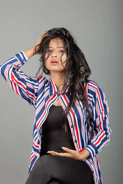 Gri stüdyo arka planında siyah, kırmızı, mavi, beyaz çizgili tunikli uzun siyah saçlı güzel bir kadın model.