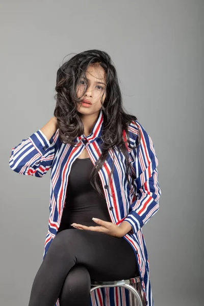 Gri stüdyo arka planında siyah, kırmızı, mavi, beyaz çizgili tunikli uzun siyah saçlı güzel bir kadın model.