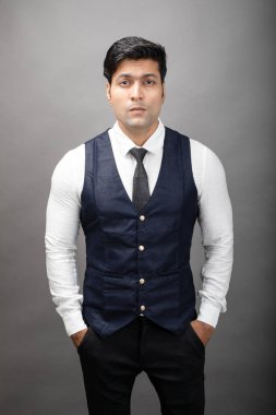 Gri arka planda resmi giyinmiş neşeli, genç ve yakışıklı Hintli iş adamının stüdyo çekimi. Erkek model. Moda Portresi.