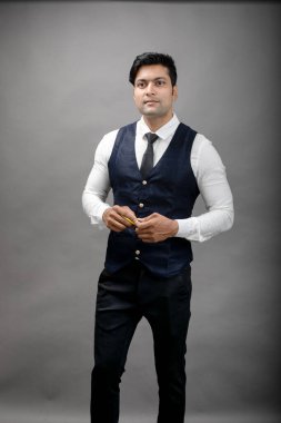 Gri arka planda resmi giyinmiş neşeli, genç ve yakışıklı Hintli iş adamının stüdyo çekimi. Erkek model. Moda Portresi.