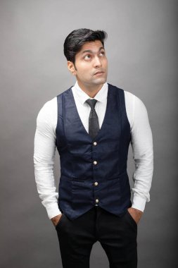 Gri arka planda resmi giyinmiş neşeli, genç ve yakışıklı Hintli iş adamının stüdyo çekimi. Erkek model. Moda Portresi.