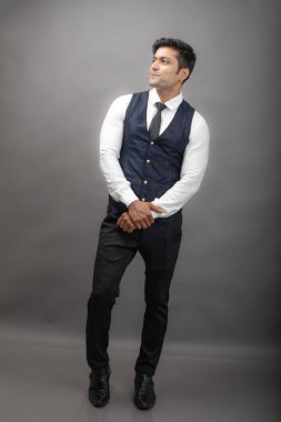 Gri arka planda resmi giyinmiş neşeli, genç ve yakışıklı Hintli iş adamının stüdyo çekimi. Erkek model. Moda Portresi.