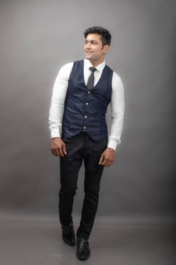Gri arka planda resmi giyinmiş neşeli, genç ve yakışıklı Hintli iş adamının stüdyo çekimi. Erkek model. Moda Portresi.