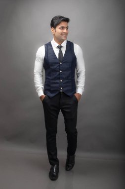 Gri arka planda resmi giyinmiş neşeli, genç ve yakışıklı Hintli iş adamının stüdyo çekimi. Erkek model. Moda Portresi.