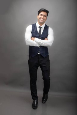 Gri arka planda resmi giyinmiş neşeli, genç ve yakışıklı Hintli iş adamının stüdyo çekimi. Erkek model. Moda Portresi.