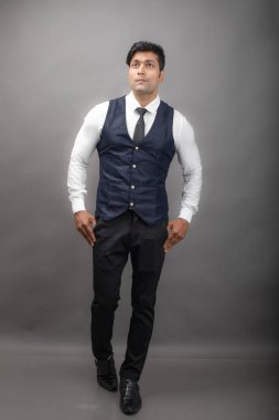 Gri arka planda resmi giyinmiş neşeli, genç ve yakışıklı Hintli iş adamının stüdyo çekimi. Erkek model. Moda Portresi.