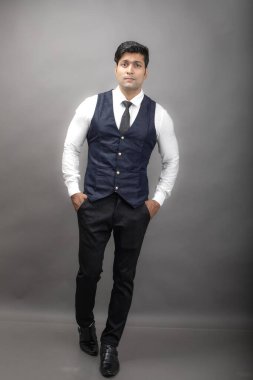 Gri arka planda resmi giyinmiş neşeli, genç ve yakışıklı Hintli iş adamının stüdyo çekimi. Erkek model. Moda Portresi.