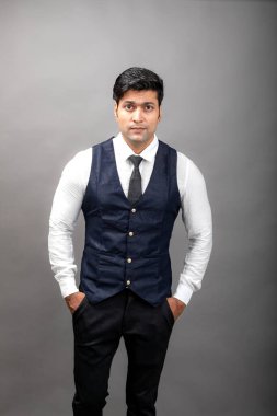 Gri arka planda resmi giyinmiş neşeli, genç ve yakışıklı Hintli iş adamının stüdyo çekimi. Erkek model. Moda Portresi.