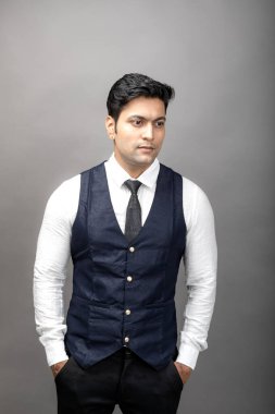 Gri arka planda resmi giyinmiş neşeli, genç ve yakışıklı Hintli iş adamının stüdyo çekimi. Erkek model. Moda Portresi.