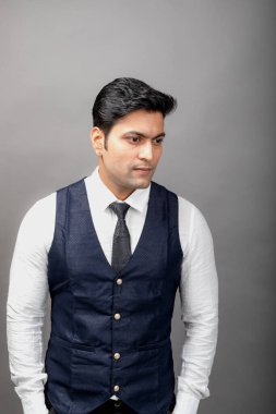 Gri arka planda resmi giyinmiş neşeli, genç ve yakışıklı Hintli iş adamının stüdyo çekimi. Erkek model. Moda Portresi.