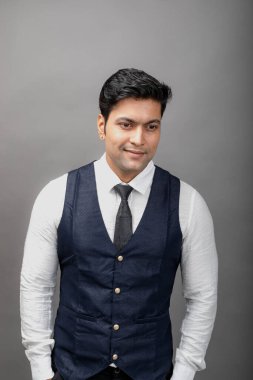 Gri arka planda resmi giyinmiş neşeli, genç ve yakışıklı Hintli iş adamının stüdyo çekimi. Erkek model. Moda Portresi.