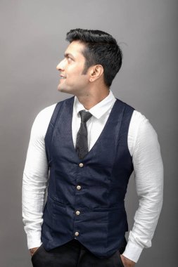 Gri arka planda resmi giyinmiş neşeli, genç ve yakışıklı Hintli iş adamının stüdyo çekimi. Erkek model. Moda Portresi.