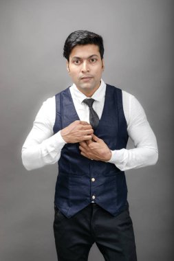 Gri arka planda resmi giyinmiş neşeli, genç ve yakışıklı Hintli iş adamının stüdyo çekimi. Erkek model. Moda Portresi.
