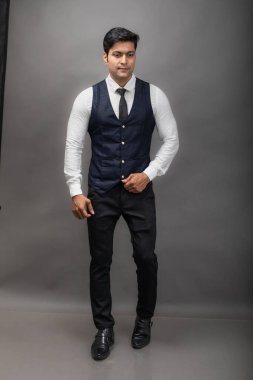 Gri arka planda resmi giyinmiş neşeli, genç ve yakışıklı Hintli iş adamının stüdyo çekimi. Erkek model. Moda Portresi.