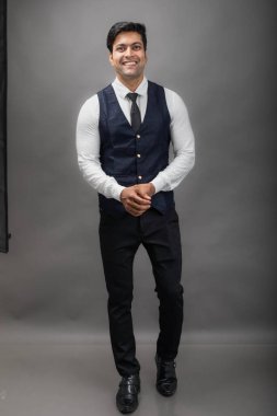 Gri arka planda resmi giyinmiş neşeli, genç ve yakışıklı Hintli iş adamının stüdyo çekimi. Erkek model. Moda Portresi.