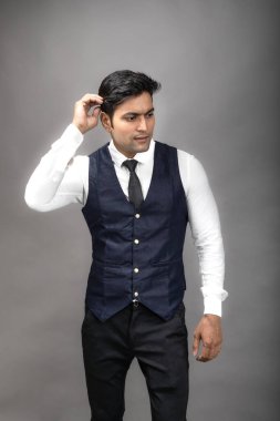 Gri arka planda resmi giyinmiş neşeli, genç ve yakışıklı Hintli iş adamının stüdyo çekimi. Erkek model. Moda Portresi.