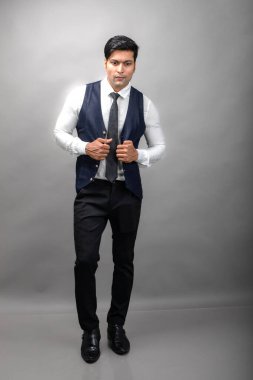 Gri arka planda resmi giyinmiş neşeli, genç ve yakışıklı Hintli iş adamının stüdyo çekimi. Erkek model. Moda Portresi.