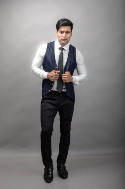 Gri arka planda resmi giyinmiş neşeli, genç ve yakışıklı Hintli iş adamının stüdyo çekimi. Erkek model. Moda Portresi.