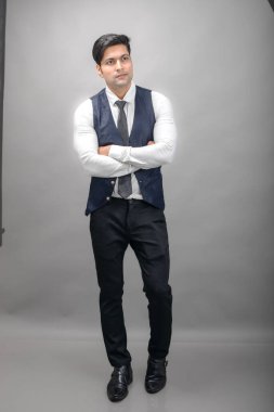 Gri arka planda resmi giyinmiş neşeli, genç ve yakışıklı Hintli iş adamının stüdyo çekimi. Erkek model. Moda Portresi.