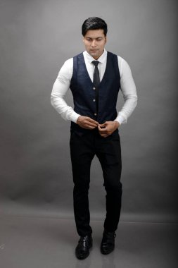 Gri arka planda resmi giyinmiş neşeli, genç ve yakışıklı Hintli iş adamının stüdyo çekimi. Erkek model. Moda Portresi.