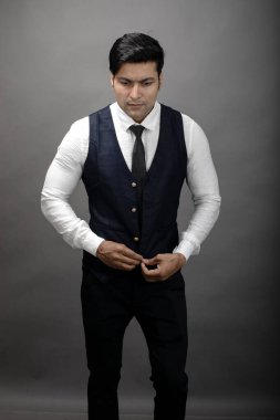 Gri arka planda resmi giyinmiş neşeli, genç ve yakışıklı Hintli iş adamının stüdyo çekimi. Erkek model. Moda Portresi.