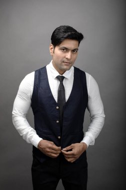 Gri arka planda resmi giyinmiş neşeli, genç ve yakışıklı Hintli iş adamının stüdyo çekimi. Erkek model. Moda Portresi.