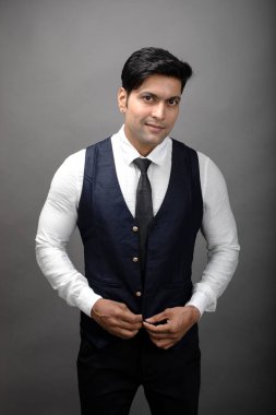 Gri arka planda resmi giyinmiş neşeli, genç ve yakışıklı Hintli iş adamının stüdyo çekimi. Erkek model. Moda Portresi.