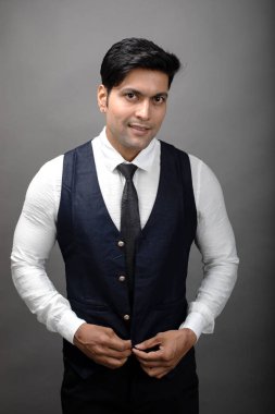 Gri arka planda resmi giyinmiş neşeli, genç ve yakışıklı Hintli iş adamının stüdyo çekimi. Erkek model. Moda Portresi.