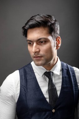 Resmi giyinmiş neşeli, genç ve yakışıklı Hintli erkek modelin atölye çekimi. Beyaz gömlek, siyah kravat, gri arka planda siyah ceket. Erkek model. Moda Portresi.