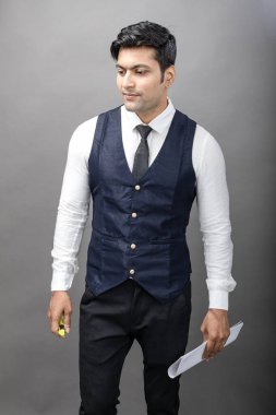 Hintli genç iş adamı resmi bir klasör üzerinde sunum yapıyor. Beyaz gömlek, siyah kravat ve gri arka planda siyah ceket giyiyor. Erkek modeli.