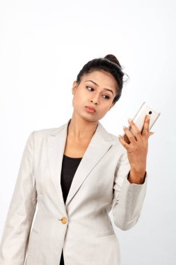 Kurumsal ofis hanımı, siyah saçlı, kalemle oynaşan, resmi olarak akıllı telefonlu beyaz ceketli beyaz arka planlı bir kadın..