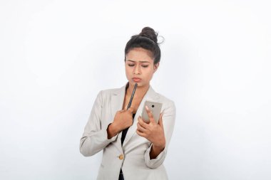 Kurumsal ofis hanımı, siyah saçlı, kalemle oynaşan, resmi olarak akıllı telefonlu beyaz ceketli beyaz arka planlı bir kadın..